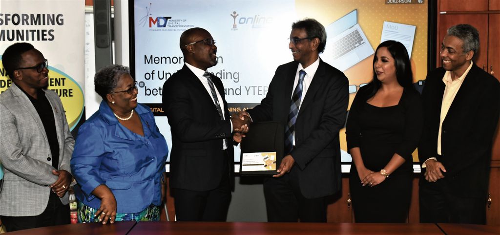 YTEPP CEO Nigel Parris, left, shakes hands with the Permanent  Secretary in the Ministry of Digital Transformation Richard Madray following the signing of a MOU to bring training to 10,000 people. Looking on are Deputy YTEPP Chairman Jesse Moss, left,  YTEPP Chairman Thora Best,  Senior Legal Officer MDT Sonya Gyan, second from right, and Deputy National Chief, Digital Officer MDT Wayne Nakhid.