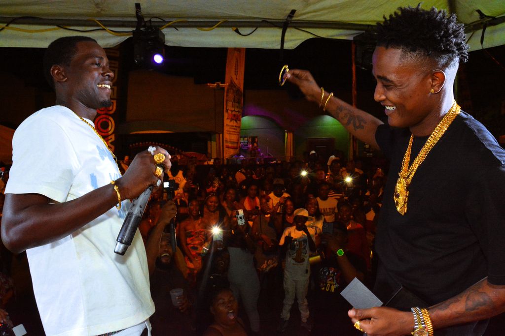 Yung Bredda (Akhenaton Lewis), right, prepares to embrace “DJ Hotty” (Jelani Hepburn) after receiving a gold wristband from him as a birthday present live on stage.