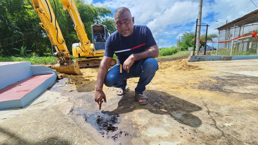 Vinesh Mahadeo points to some oil remnants in the yard of his home. (Photo by Kristian De Silva)